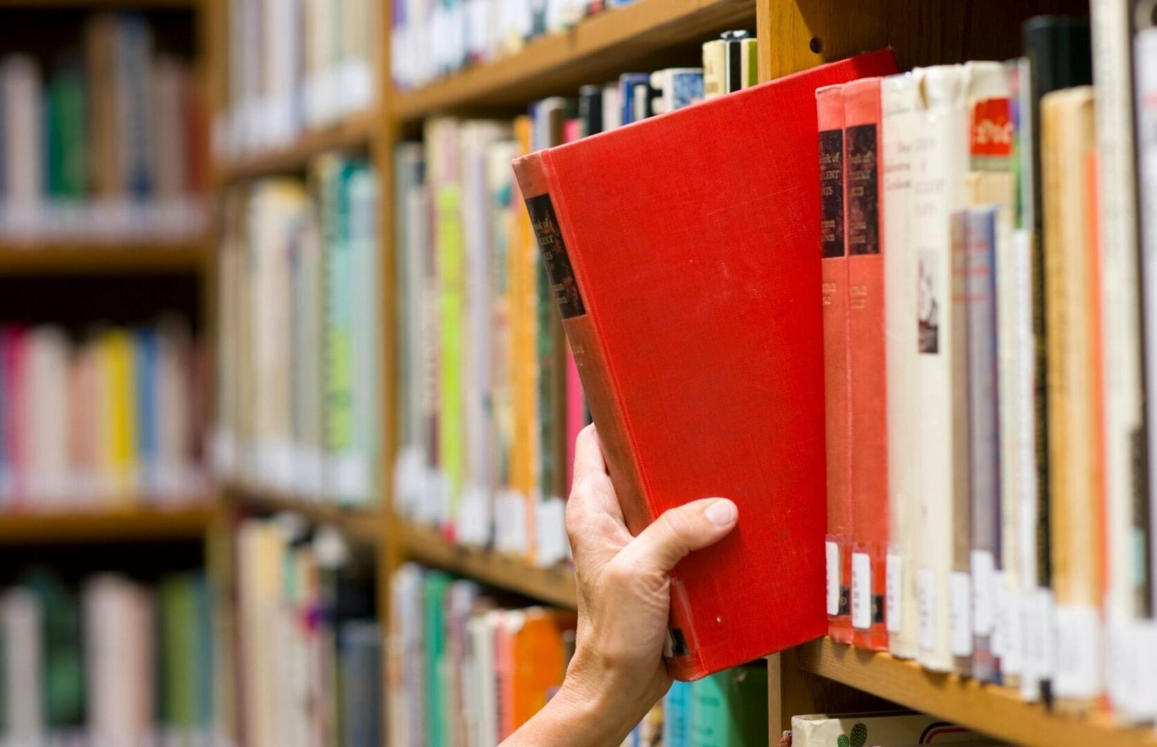 A person holding onto a red book in front of some books.